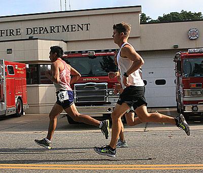 Angel Rojas and Jason Hancock, passing in front of the Springs firehouse above, were to finish second and third in Labor Day’s 10K.