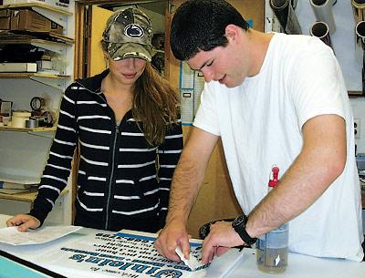 Jacqulene Albright-Kehoe, whose father, Jack Kehoe, opened Sign Language in 1979, looked over lettering being done by her cousin Sean Kehoe.