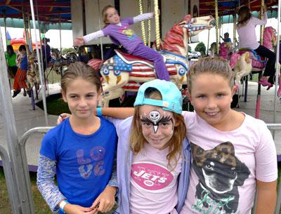 Maisie Noll, Sofia Nagle, and Maggie Nordlinger posed for a photo as Nina D’Agostino rode by on the carousel.