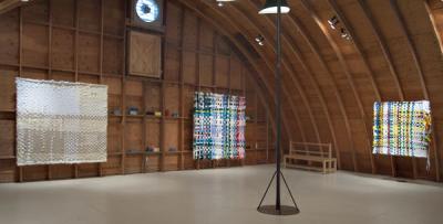 Although Louise Eastman’s woven fiberworks have been mounted on board to hang appropriately in the arched, unfinished rafters of the gallery’s loft, they normally hang without backing.