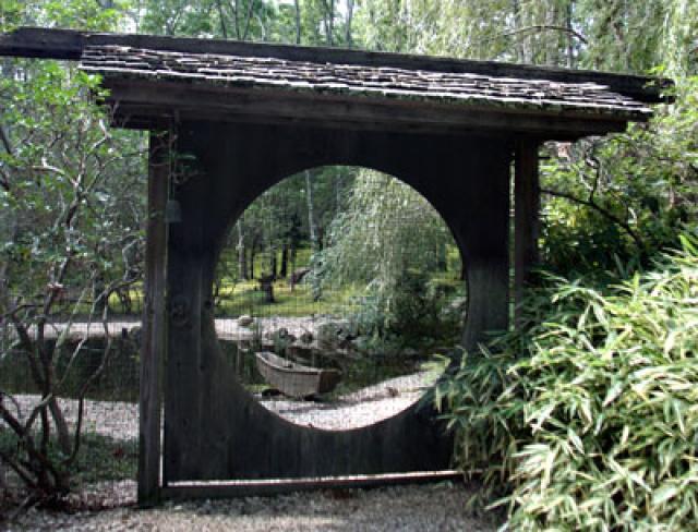 Through a gate from an old Chinese castle on a 20-acre wooded property in East Hampton, a marsh boat can be seen on the shore of a koi pond. The homeowner likes to let structures age and develop a patina.