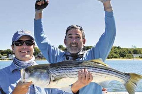 Chris Lanning, arms raised in celebration, caught this 35-inch striper in three feet of water off of Shelter Island last week while fishing with his guide Brendan McCarthy.