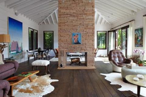 A two-story stone fireplace divides the living room. The art is by Dirk Skreber, left wall, George Condo, fireplace, and Herman Bas, right wall. The coffee table, left foreground, is by George Nakashima. Vintage American armchairs covered in linen, below, are beneath a Massimo Vitali photograph in the master bedroom.