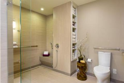 This model bathroom for aging-in-place has grab bars and an open, curbless shower with a sturdy seat and a hand-held shower head. (The plant stand was put in place by the unknown photographer.)