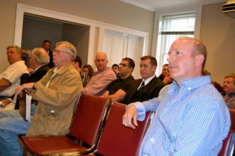 Sag Harbor Police Officer David Driscoll, right, listened in at a Sag Harbor Village Board meeting where the mayor and audience debated the elimination of his position on the force.