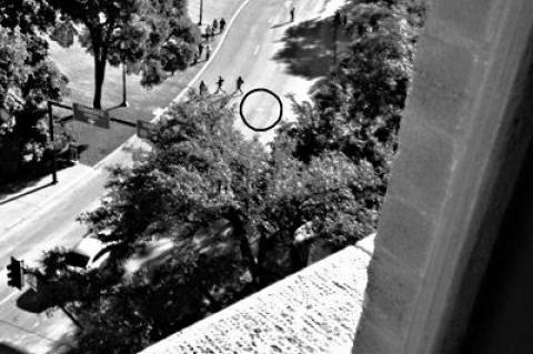 This corner window on the seventh floor of the Texas School Book Depository Building is directly above the window on the sixth floor from which Lee Harvey Oswald fired at the president. The circle imposed on the pavement below marks one of two white Xs that commemorate exactly where he was hit.