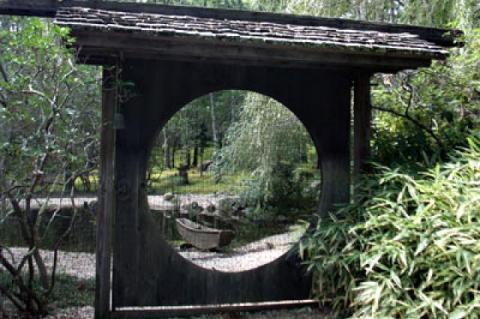 Through a gate from an old Chinese castle on a 20-acre wooded property in East Hampton, a marsh boat can be seen on the shore of a koi pond. The homeowner likes to let structures age and develop a patina.